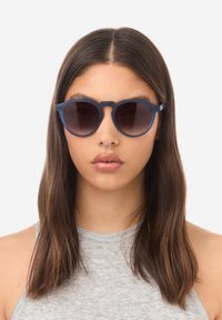 Kulaté sluneční brýle s matným námořnicky modrým rámečkem a tmavými gradientními čočkami, s jedinečným designem mostu. Lehký a moderní vzhled.