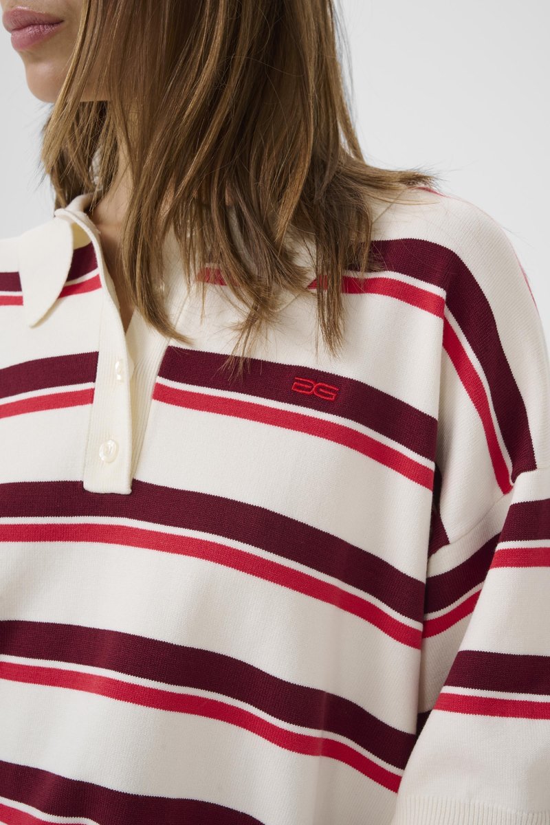 Woman wearing a white collared shirt with horizontal red and burgundy stripes and a small red "DG" logo on the chest.