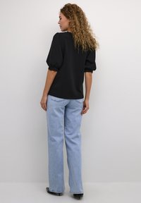 Black puff-sleeve top with a round neck, paired with high-waisted light blue jeans. Both garments have a relaxed fit and smooth texture.
