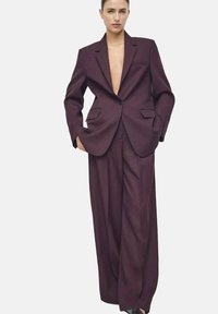 Costume ajusté violet foncé composé d'un blazer structuré avec des revers et d'un pantalon large taille haute, avec des poches latérales et des lignes épurées.