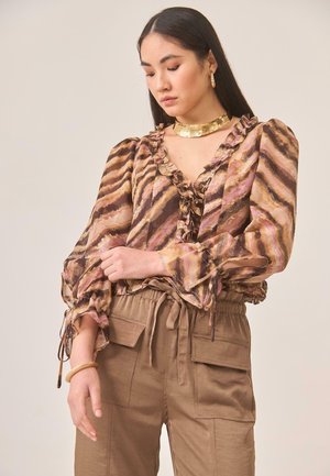 Blusa sheer multicolorida con patrón ondulado en marrones, rosas y dorados; con cuello y mangas acampanados; combinada con pantalones cargo en tono marrón claro.