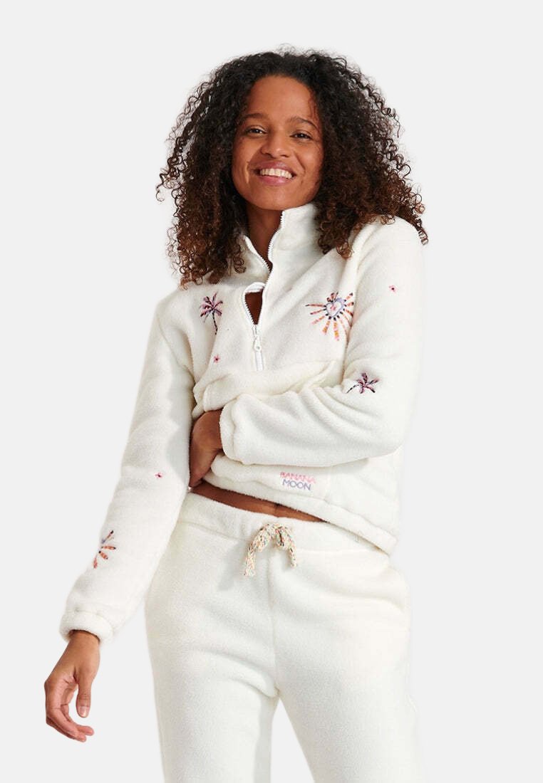 Pullover in pile bianco sporco con apertura a zip sulla metà, ricami floreali e polsini a coste. Abbinato a pantaloni coordinati con coulisse.