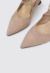 Bailarinas de ante beige con punta afilada, que cuentan con un tacón bajo y un detalle de tiras entrecruzadas sobre el empeine, un forro interior suave y un diseño minimalista.