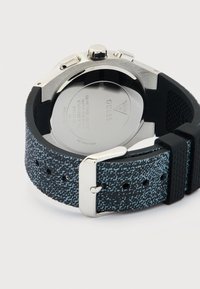 Montre-bracelet avec dos en métal, bracelet texturé noir et bleu et boucle en argent, affichant la résistance à l'eau et le logo de la marque gravé.