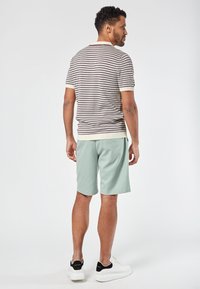 Raidoitu neulepolo pusero beige-, ruskea- ja valkoisilla väreillä, yhdistettynä vaaleanvihreisiin shortsihousuihin. Valkoiset tennarit mustilla yksityiskohdilla.