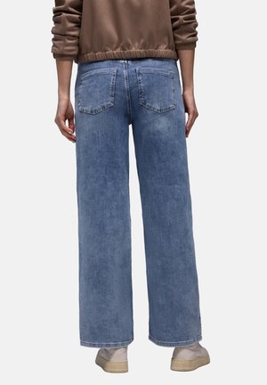 Hellblaue Jeans mit weitem Bein aus Denim, mit zwei Gesäßtaschen und lockerem Schnitt, kombiniert mit einem braunen Oberteil mit elastischem Bund.