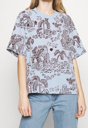 Chemise bleu clair à manches courtes avec des motifs de croquis tropicaux et urbains brun foncé, portée avec un jean bleu clair.