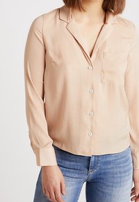 Light pink, long-sleeve button-up shirt with a pocket, soft fabric, classic collar, and straight hem, paired with blue jeans.