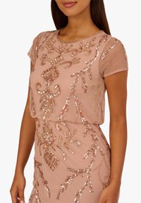 Robe rose poudré ornée de perles avec manches courtes, présentant une broderie florale complexe et des sequins sur un tissu transparent, offrant une texture et un motif délicats.