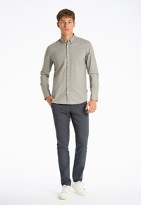 Camicia grigia con colletto, abbinata a pantaloni scuri e sneaker bianche. Tessuto liscio, nessun motivo visibile e branding minimale.