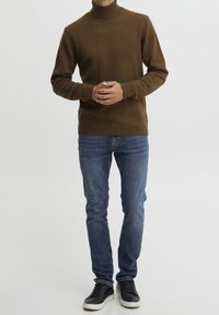 Pull à col roulé marron ajusté en matière douce, associé à un jean bleu en denim et des baskets noires, présenté en vue de face.