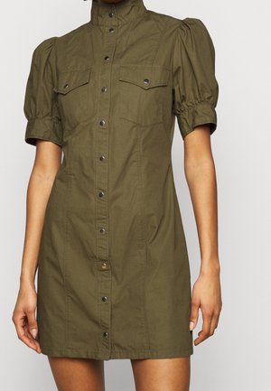 Abito corto verde oliva con maniche a sbuffo, collo alto e chiusura frontale con bottoni. Presenta due tasche sul petto e una silhouette aderente.