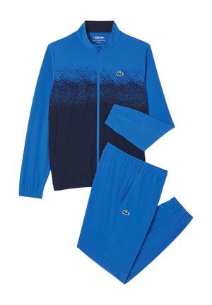 Niebieski dres z zapinaną na zamek kurtką z gradientowym wzorem, kontrastującą granatową dolną częścią oraz dopasowanymi spodniami z elastycznym pasem.