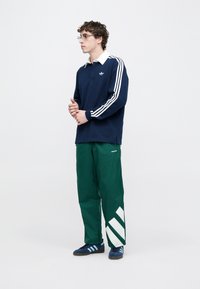 Tengeri kék hosszú ujjú póló fehér gallérral és három fehér csíkkal az ujjakon, zöld nadrággal fehér ferde csíkokkal. Kék cipő.