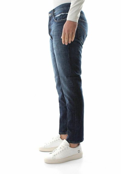 Jeans in denim blu scuro, di taglio dritto con dettagli consumati, abbinati a sneakers bianche. Texture liscia con dettagli di cucitura visibili.