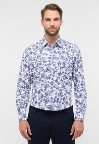 Wit katoenen overhemd met lange mouwen en een blauw bloemmotief. Voorzien van een button-down kraag en contrasterende marineblauwe broek.