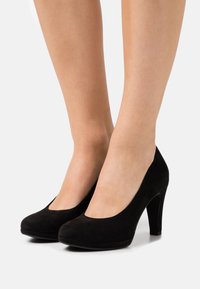 Černé semišové lodičky na vysokém podpatku s kulatou špičkou a hladkým povrchem. Zvýšený podpatek pro větší výšku a stabilitu.