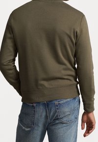 Sudadera verde oliva con cuello redondo y puños acanalados, combinada con vaqueros azul denim. Tejido suave y corte holgado.