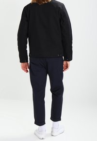 Černá bavlněná bunda s rovného střihu a knoflíkovými akcenty, spárovaná s námořnickými kalhotami a bílými teniskami, s ohrnutými lemy a texturovanou látkou.