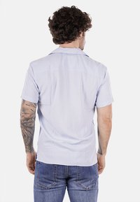 Camicia azzurro chiaro a maniche corte realizzata in tessuto leggero, con colletto e dettagli sottili sulla yoke posteriore. Indossata con jeans.