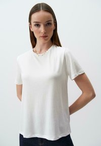 T-shirt bianco a maniche corte con vestibilità rilassata, texture liscia, scollo rotondo e design minimalista, abbinato a una collana delicata.