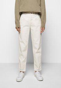 Białe bawełniane jeansy o prostym kroju z wysokim stanem. W połączeniu z beżowym swetrem z dzianiny i białymi trampkami, posiadającymi widoczne logo marki na dolnej krawędzi.