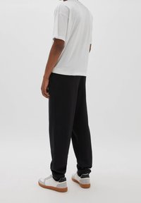 Vit kortärmad t-shirt, avslappnad passform, kombinerad med svarta lösa sweatpants och vita sneakers med grå och svarta detaljer.