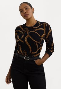 Maglione nero con un motivo a catena dorata, scollo rotondo e maniche lunghe. Abbinato a jeans neri a vita alta e una cintura nera.