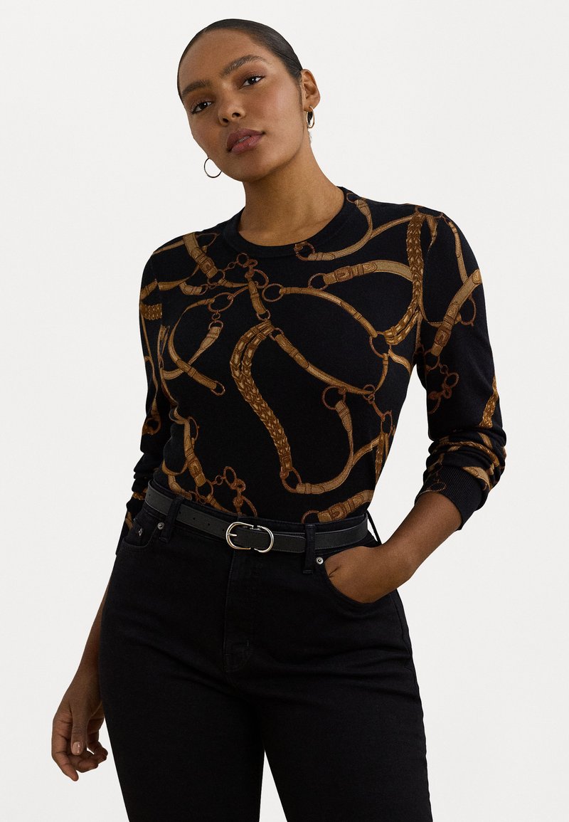Maglione nero con un motivo a catena dorata, scollo rotondo e maniche lunghe. Abbinato a jeans neri a vita alta e una cintura nera.