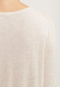 Pull couleur crème avec un tricot doux et texturé. Il présente un large décolleté et des coutures d'épaule légèrement tombantes. Design simple et minimaliste.
