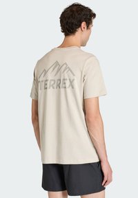 Jasnobeżowa bawełniana koszulka z grafiką szarej góry i napisem "TERREX" na plecach. Krótkie rękawy i luźny krój.