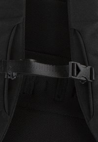 Innenraum eines schwarzen Stoffrucksacks mit einem strukturierten Netzpanel und einem verstellbaren Riemen mit einer Kunststoffschnalle für sicheren Verschluss.