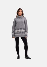 Maglione grigio oversize con collo alto a coste, caratterizzato da un motivo bianco lungo l'orlo, abbinato a leggings neri e scarpe.