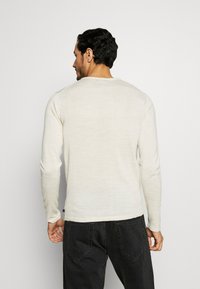 Hosszú ujjú, crew neck pulóver világos bézs anyagból, puha tapintása és testhezálló fazonja van, sötét farmernadrággal párosítva.