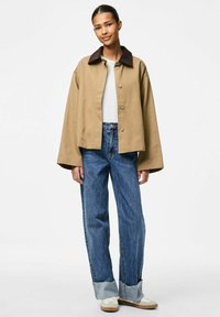 Bežna skrajšana jakna z rjavim ovratnikom, v kombinaciji z širokimi modrimi kavbojkami z raztrganimi robovi in belimi supergami. Minimalističen dizajn.