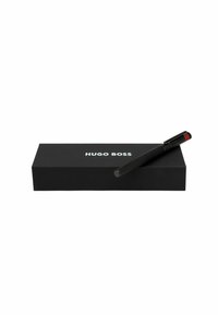 Zwarte Hugo Boss-pen met een gestructureerde grip en een rode accentkap, gepositioneerd op een bijpassende zwarte doos met een reliëf logo in witte tekst.