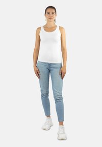 Weißes Tanktop, taillierte Form, kombiniert mit hellblauen Jeans. Das Model trägt weiße Sneakers. Einfaches Design, keine sichtbaren Muster oder Akzente.