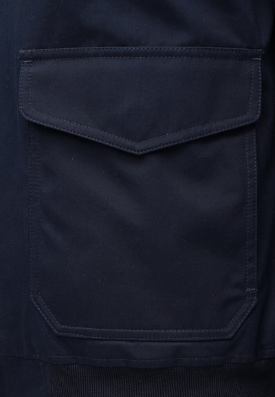 Mornarsko modra tkanina z velikim pravokotnim žepom z všitimi robovi. Gladek tekstura z rahlim leskom.