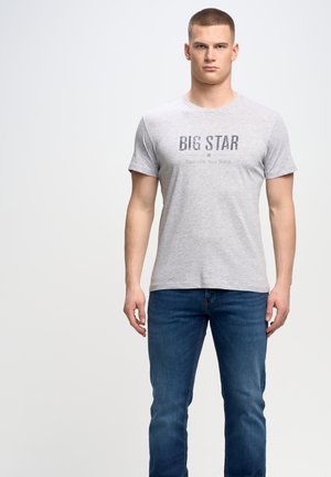 Pilkas medvilnės marškinėliai su trumpomis rankovėmis, ant kurių tamsiai pilku tekstu užrašyta "BIG STAR". Derinami su mėlynomis džinsinėmis kelnėmis. Paprastas, kasdienis dizainas.