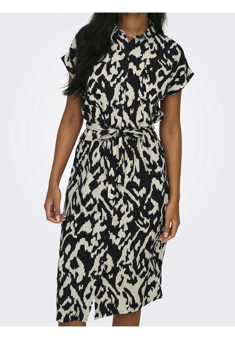Femme portant une robe boutonnée à manches courtes avec une ceinture nouée à la taille, imprimée d'un motif abstrait noir et blanc.
