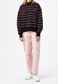 Suéter de rayas negras con líneas horizontales rosas, combinado con pantalones cargo rosa claro con bolsillos laterales y zapatillas blancas.