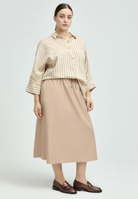 Striped beige shirt with a buttoned placket, paired with a solid beige midi skirt and metallic brown loafers. Smooth fabric texture.