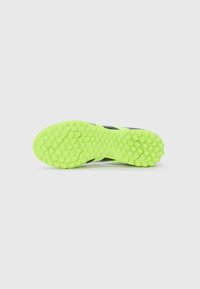 Suela de zapato deportivo negra con una base de goma verde neón brillante. Presenta patrones de agarre hexagonales texturizados para mayor tracción.