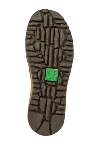 Suela de zapato de goma negra con un patrón texturizado de surcos profundos y secciones elevadas, que presenta un pequeño logo en forma de rana verde en el centro.