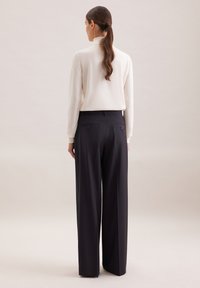 Jasny kremowy golf połączony z wysokimi, szerokimi spodniami w kolorze granatowym, charakteryzującymi się gładką teksturą i podwójnymi tylkami kieszeniami z guzikami.