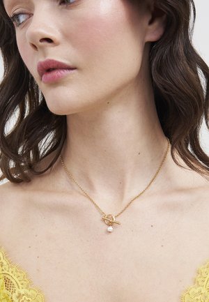 Mujer con los hombros descubiertos luciendo un delicado collar de cadena dorada con un cierre de barra y un pequeño colgante de perla única.