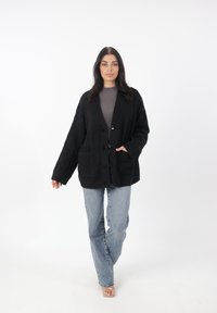 Cardigan nero lavorato a maglia dal fit morbido, con scollatura a V, chiusura con bottoni e due tasche frontali, abbinato a jeans blu chiaro.