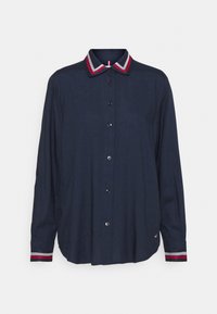 Marinblå skjorta med knappar och kontrasterande randig krage och manschetter. Mjuk tyg, avslappnad passform, har svarta knappar och subtil branding på fållen.