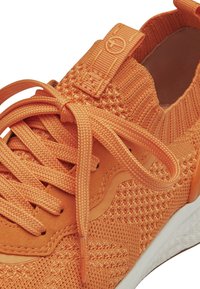 Oranges Sport-Schuh mit einem gestrickten Obermaterial, strukturierten Schnürsenkeln und seitlichen Akzenten, einer Zuglasche an der Ferse und einer weißen Gummisohle.