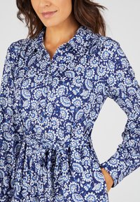 Abito floreale blu con colletto, maniche lunghe e vita regolabile con lacci. Presenta un motivo floreale bianco su fondo navy.